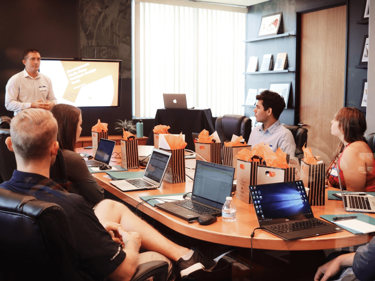 People seated around a meeting table having a discussion with laptops open